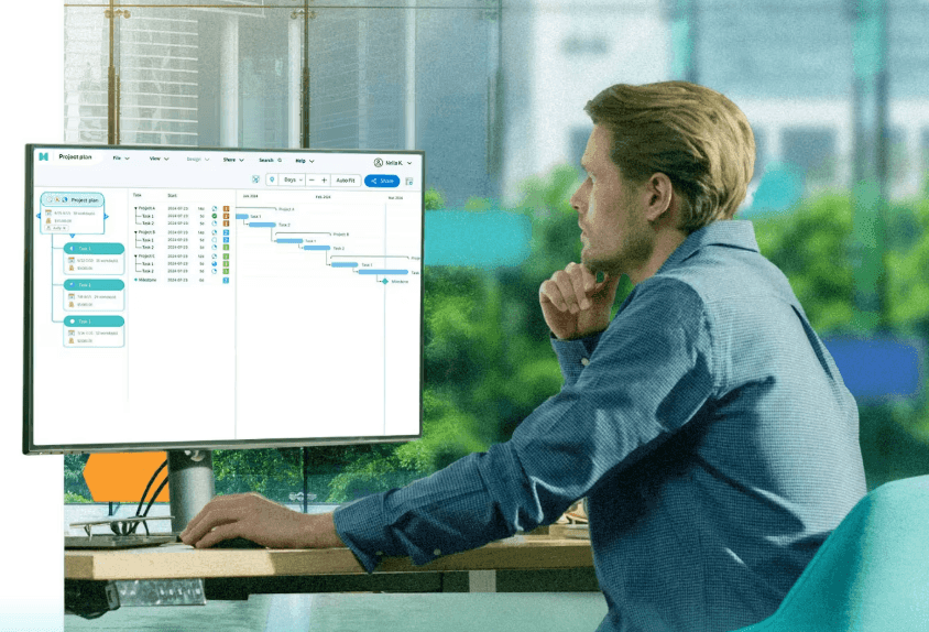 Man working at a desk viewing a Gantt chart on a computer screen in an office setting.