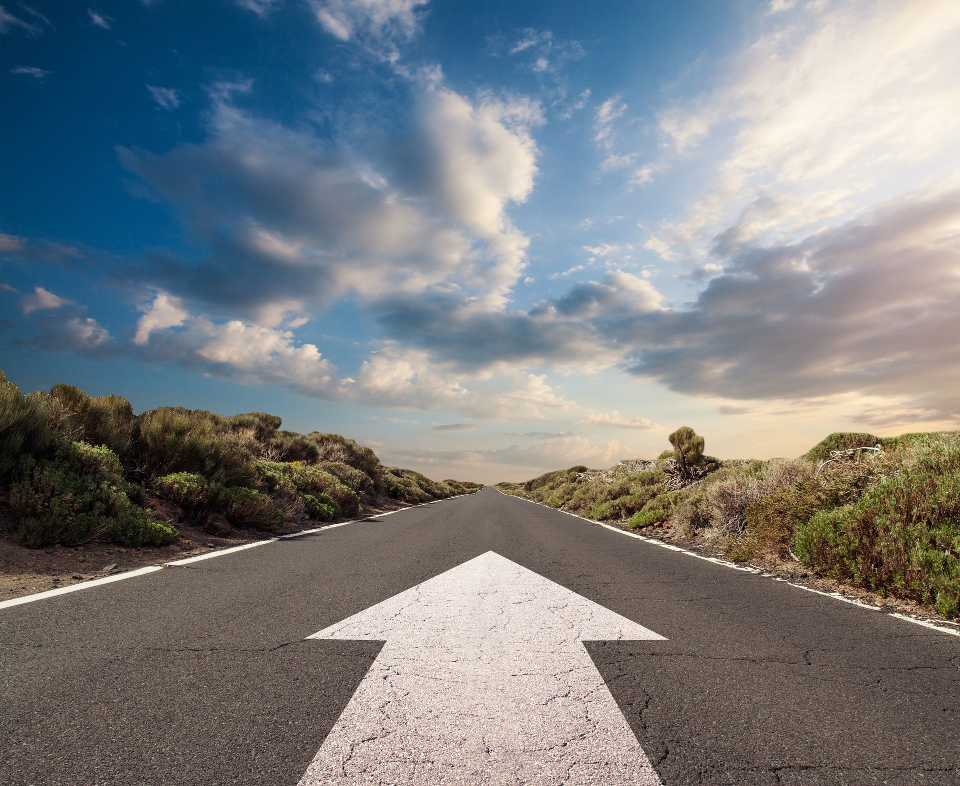 Blue sky with clouds and country road with white arrow